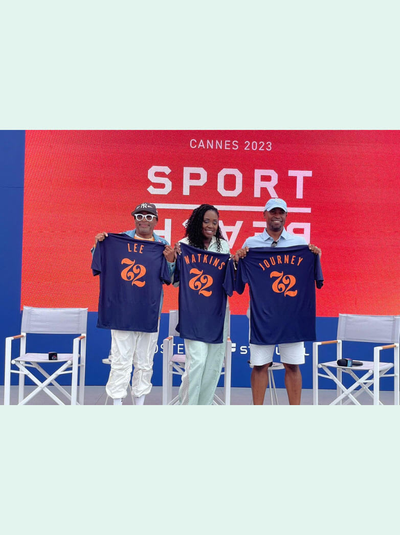 Three individuals holding personalized jerseys with a bright red event backdrop that reads "Cannes 2023 Sport Beach."