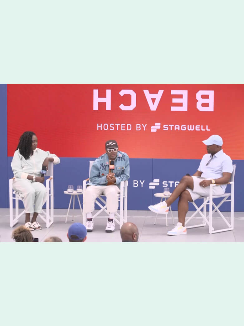 Three speakers seated in director chairs on a stage with a red backdrop reading "BEACH" hosted by Stagwell.