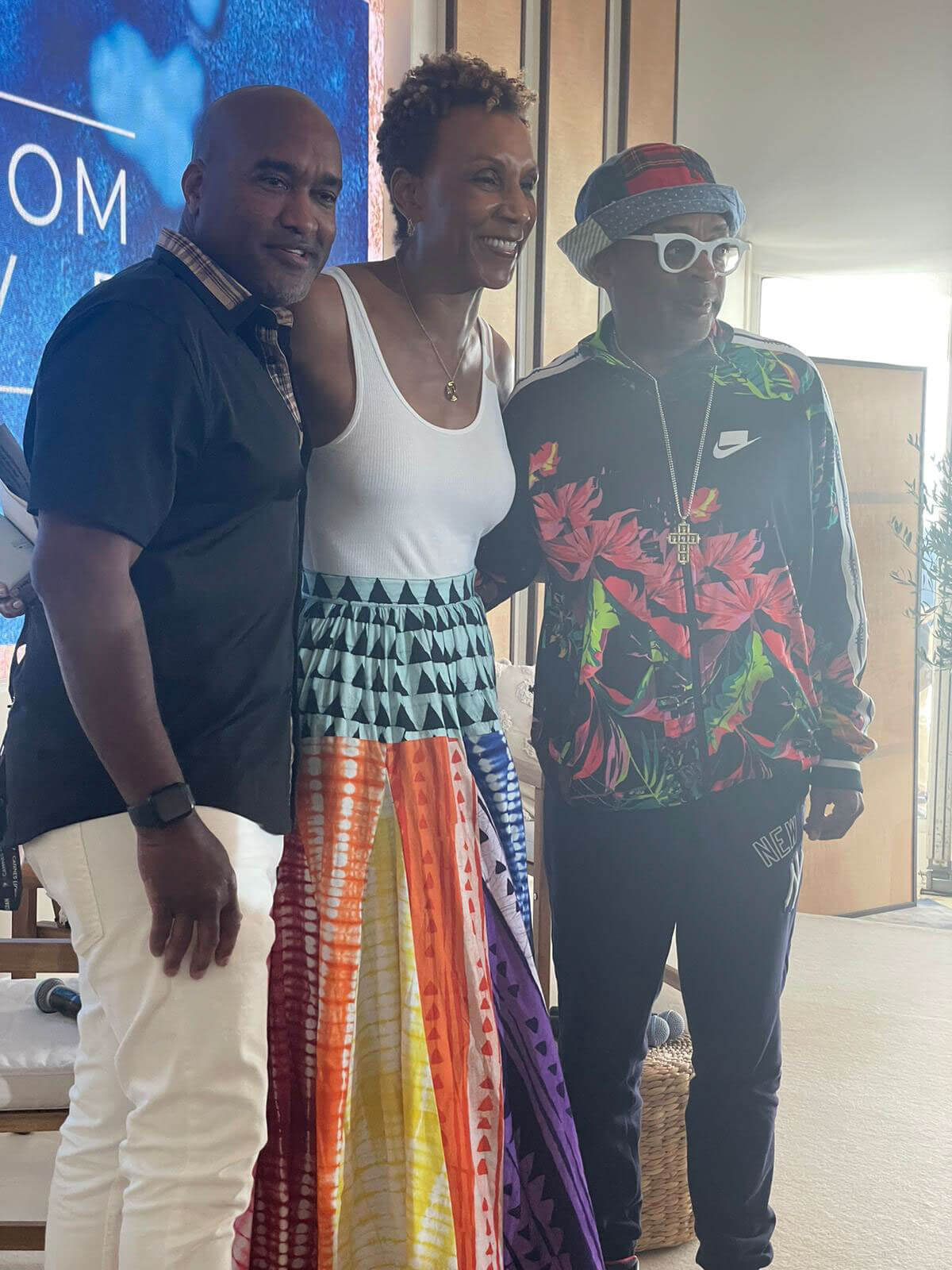 Three individuals standing and smiling together indoors, with a colorful event backdrop.