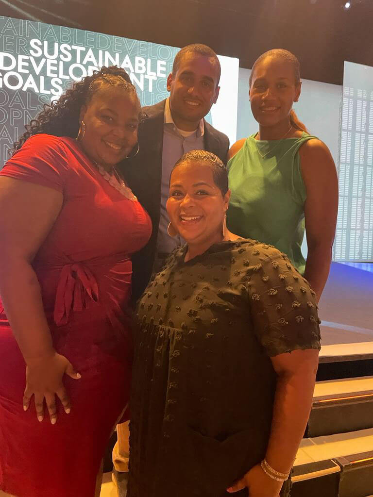 Four individuals posing together on a stage, smiling, with "Sustainable Development Goals" text displayed in the background.
