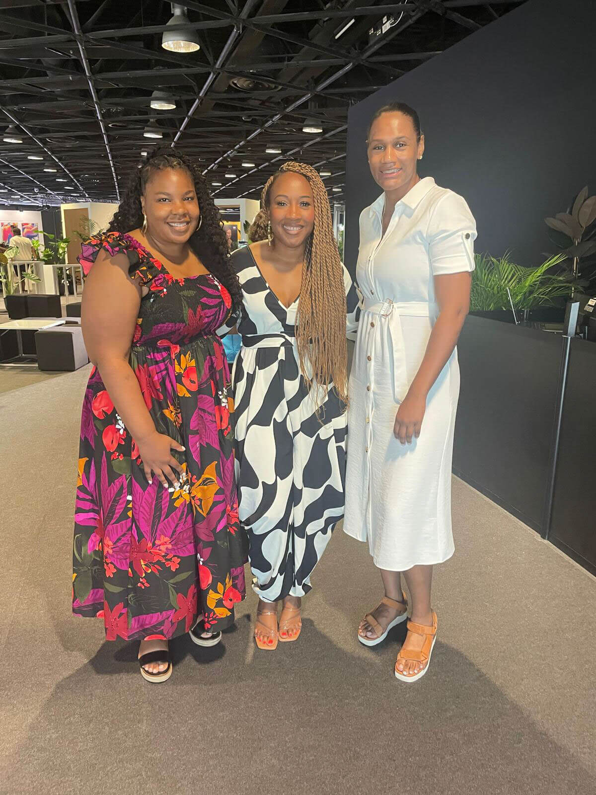 Three women standing together, smiling, in a spacious venue with modern decor.
