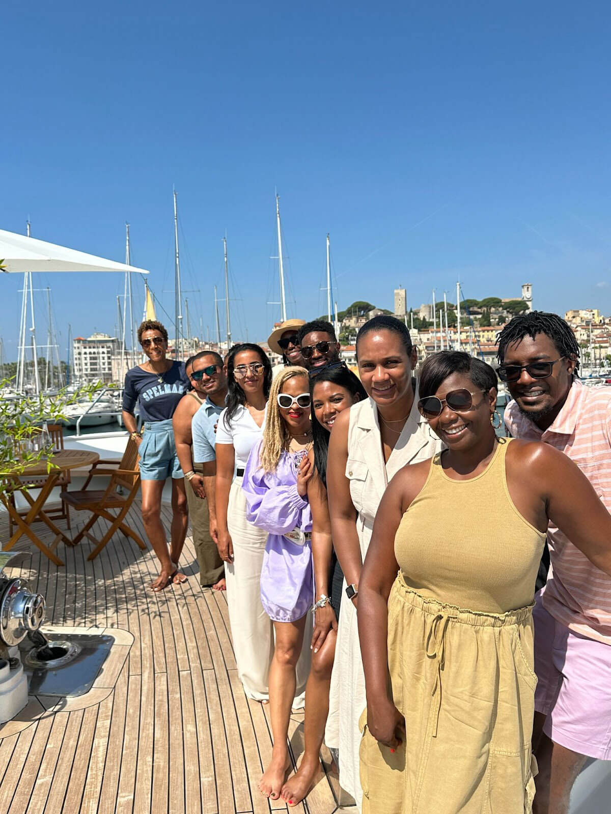 A group of people posing on a docked boat under a clear blue sky, with marina and cityscape views in the background.