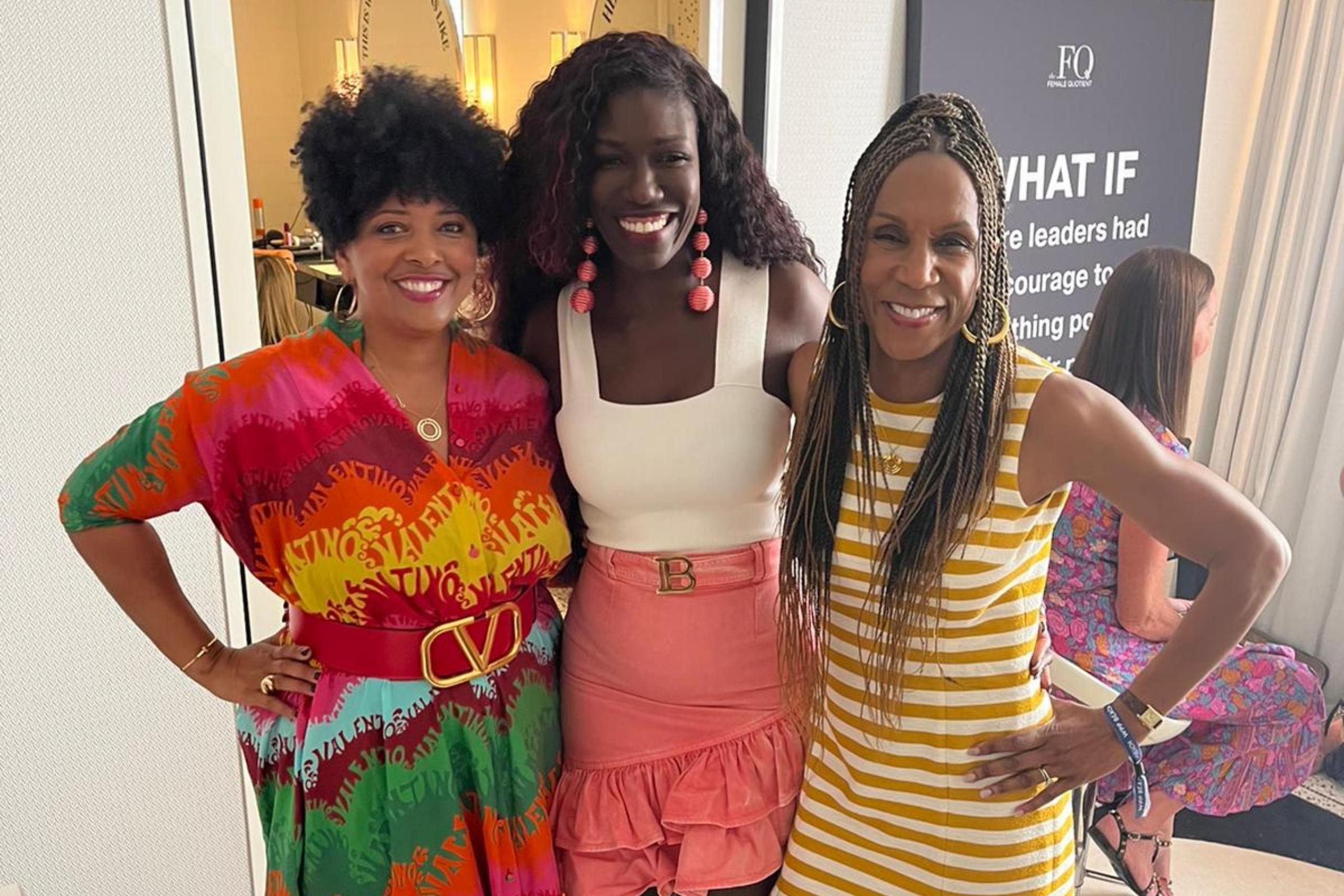 Three women smiling and posing together indoors, wearing bright and colorful outfits, exuding a sense of unity and joy.