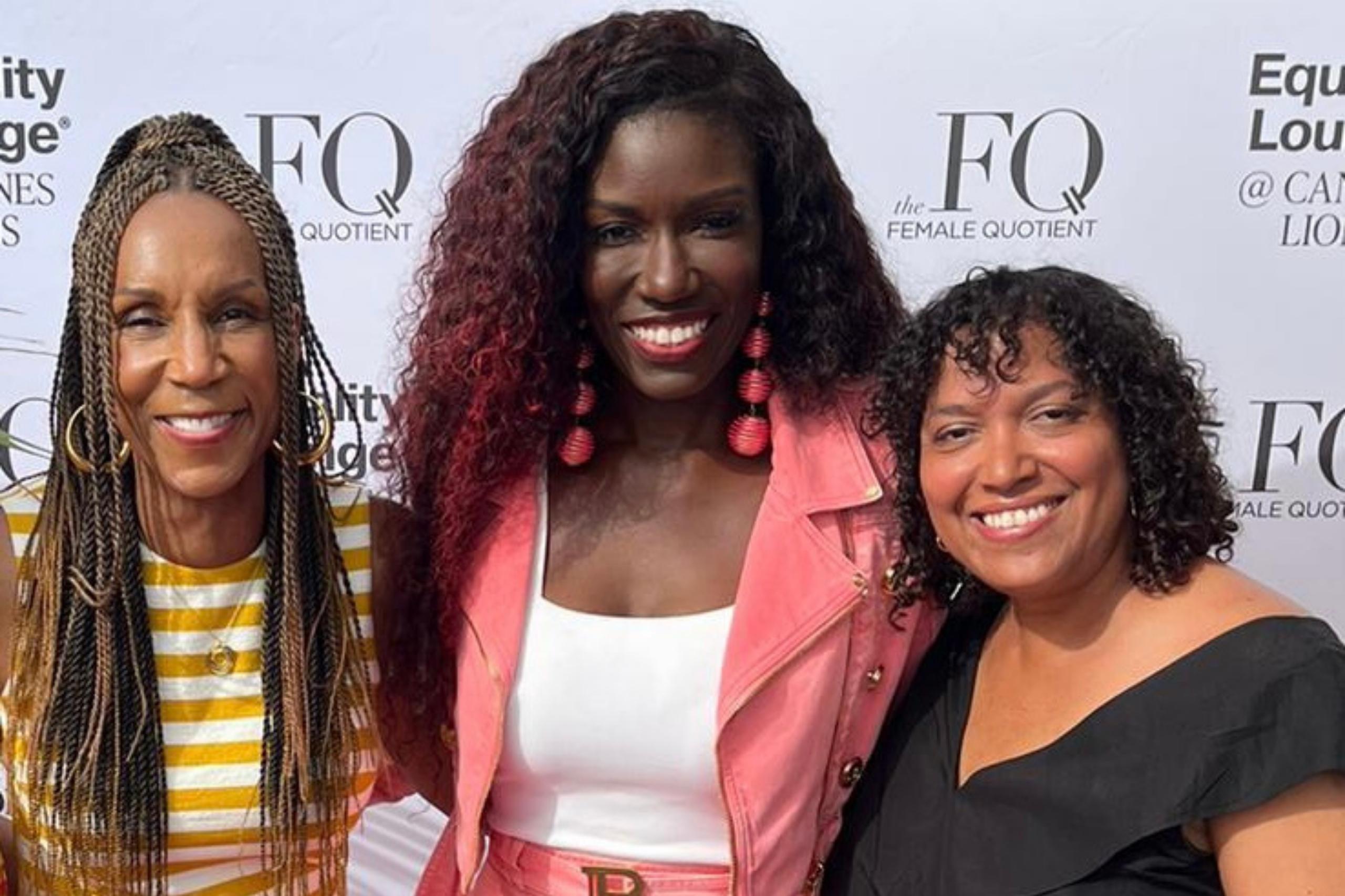 Three women posing together against a white backdrop featuring "The Female Quotient" and "Equality Lounge" logos, exuding elegance and confidence.