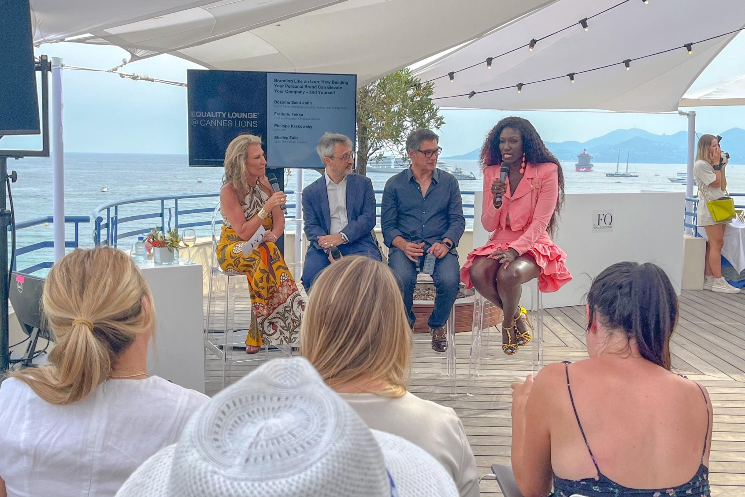 Another angle of the same outdoor panel discussion. Panelists are engaged in conversation with microphones, while attendees listen attentively. The background features the ocean, boats, and a sunny sky.