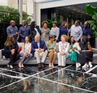 group of people seated on a sofa and standing around it, chatting and laughing in an upscale lobby area.