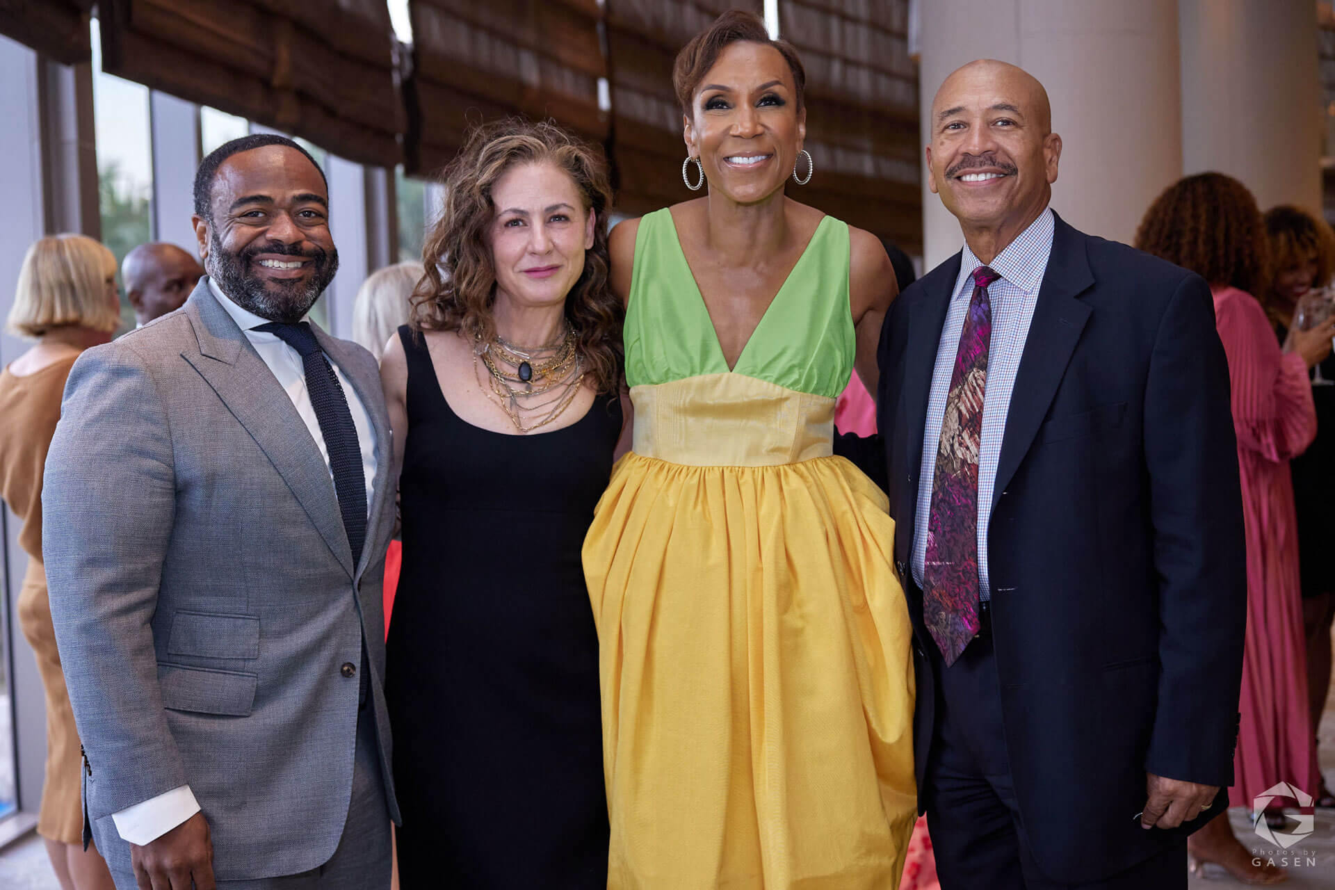A group of four people posing, including two men in suits and two women in dresses, with one woman wearing a yellow and green gown.