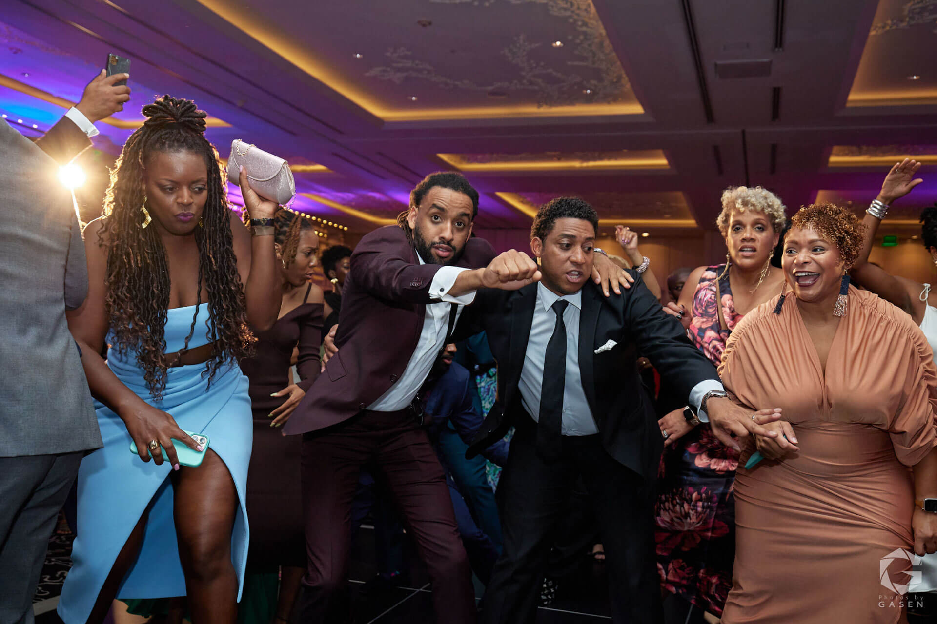 A group of attendees energetically dancing together, with a mix of determined and joyful expressions in a lively ballroom setting.