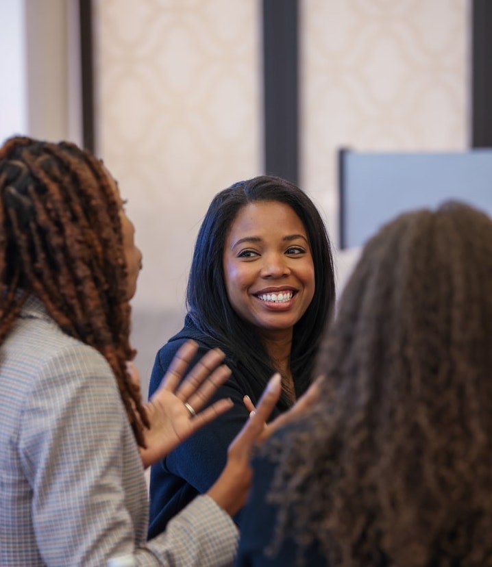 A woman with long dark hair smiling while listening to two colleagues during a discussion.