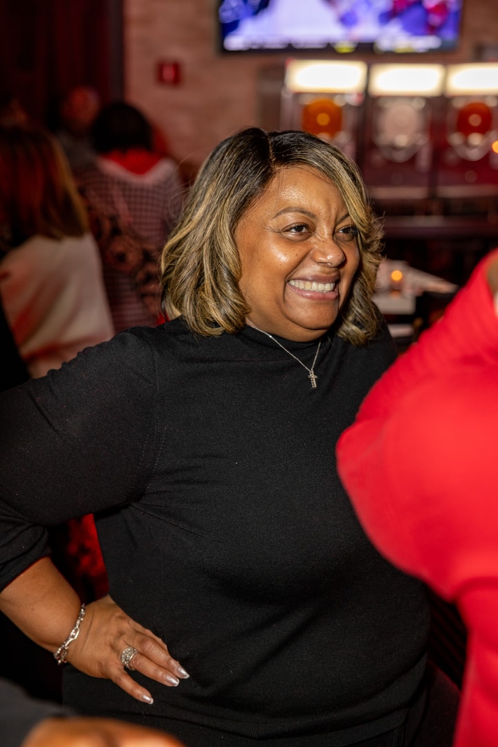 A woman with a black sweater on smiles while conversing with a colleague at Brooklyn Chop House.