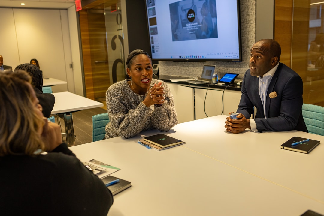 A woman in a gray sweater talking with a man in a blue blazer, seated at a table.