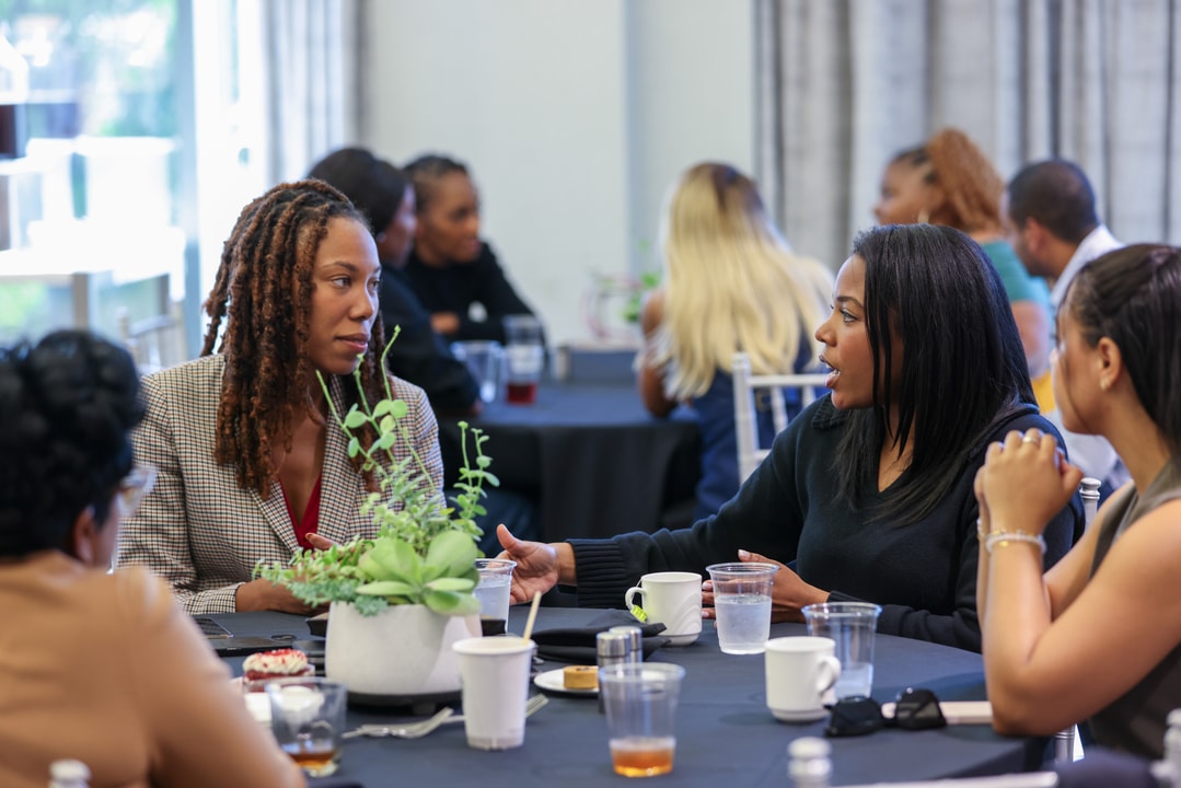 Two seated women talk while two others listen in.
