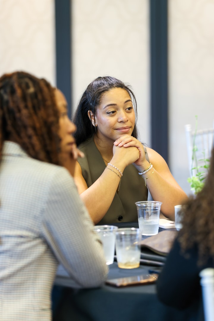 A woman in a green top listens intently as her colleague talks at the BECA Future Leaders Luncheon.