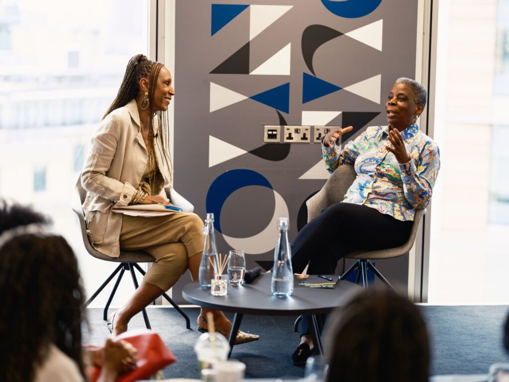 A man in a check-patterned blazer chats with a woman in a gray jacket at a networking event.